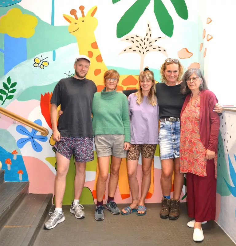 bunt bemalter Flur der LuBa Uelzen Grundschule, im Vordergrund stehen die Künstler und die Direktorin