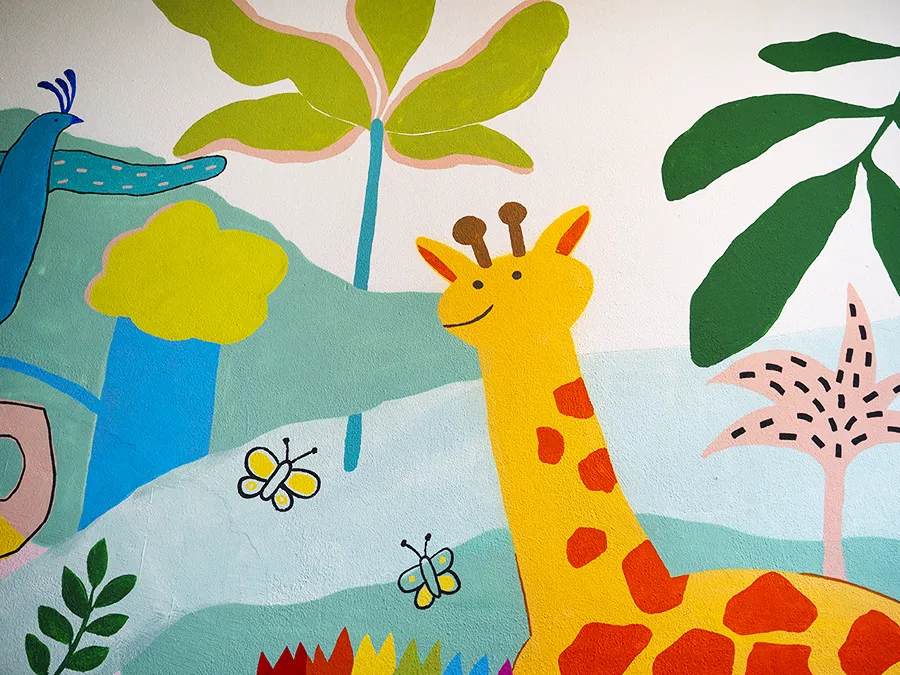 zeigt eine Wandmalerei der Lukas-Backmeister-Schule, ein buntes Bild mit einer Giraffe und Pflanzen und einem Fluss.