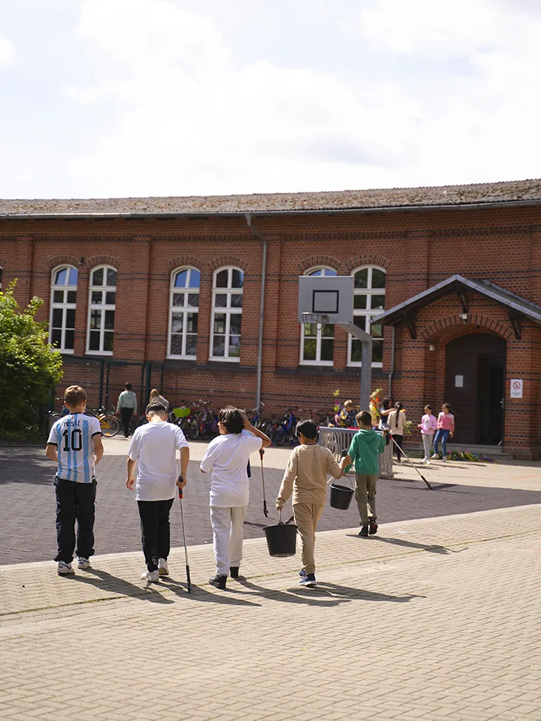 zeigt den Schulhof der Lukas-Backmeister-Schule mit Kindern. Im Hintergrund das rote Backsteingebäude.