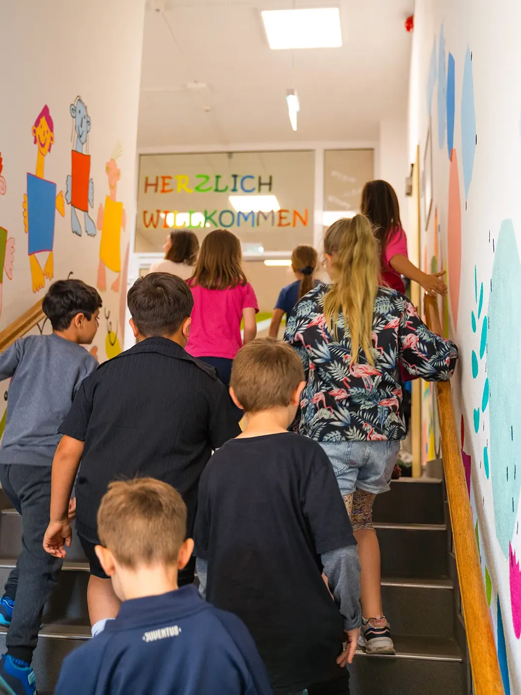 Kinder im Treppenhaus der Luba-Schule, von hinten gezeigt, mit bunten Wandmalereien