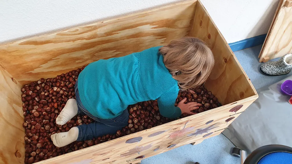 zeigt ein Kind in der Ergotherapie in einer Kiste voller Kastanien