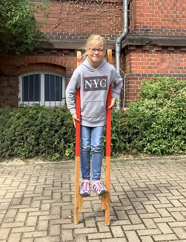 zeigt ein Kind auf Stelzen auf dem Schulhof der Luba-Ulzen